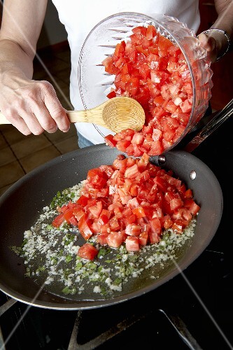 Woman Adding Fresh Diced Tomatoes into a Skillet on the Stove
