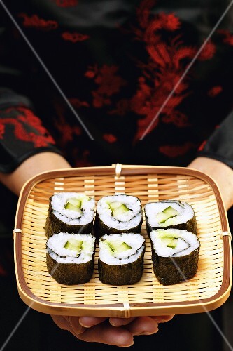 Asian woman holding maki-sushi on wicker tray