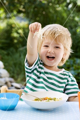 Small boy putting grated cheese into his vegetable soup