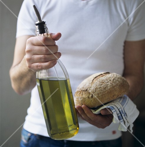 Man holding a bottle of olive oil and a loaf of bread