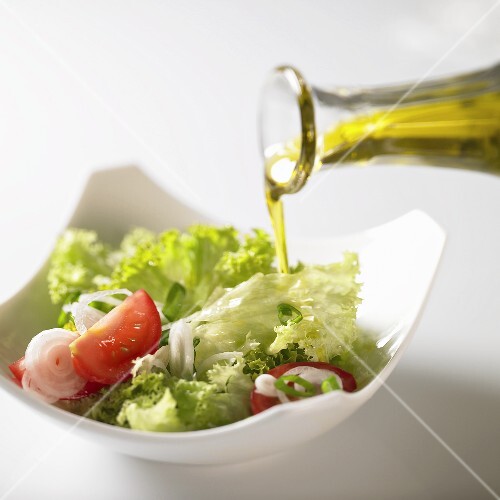 Pouring olive oil over salad leaves with tomatoes