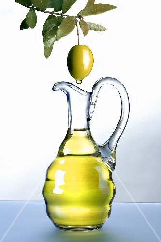 Olive oil dripping from an olive into a carafe