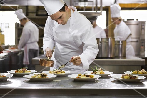 Chef spooning sauce over main courses