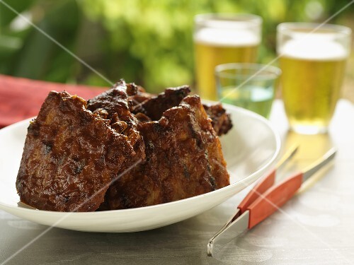 Grilled spare ribs on table out of doors, beer in background
