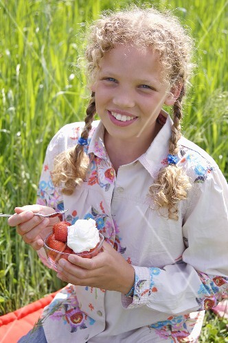 Girl eating strawberries and cream out of doors