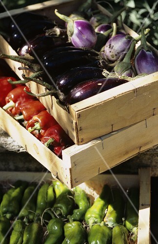 Fresh aubergines and peppers in wooden boxes