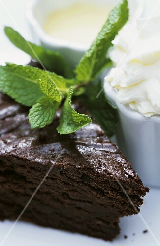 A piece of chocolate cake, fresh mint, whipped cream
