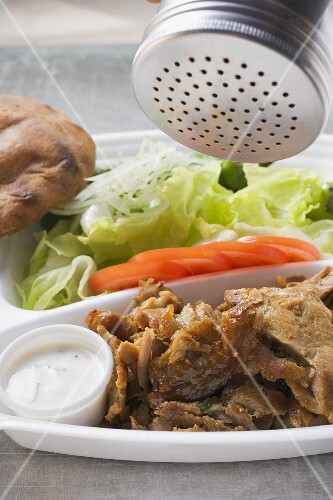 Sprinkling seasoning on döner kebab on lunch tray