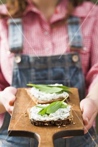 Person holding wholemeal bread with quark & ramsons on board
