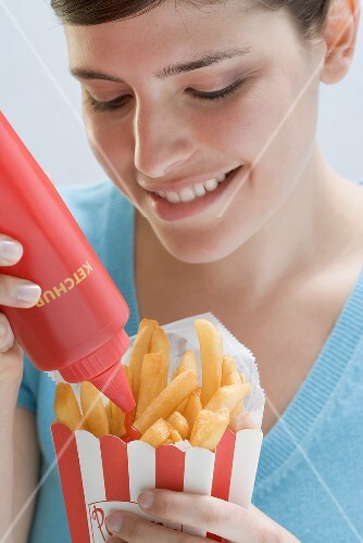 Young woman squeezing ketchup out of bottle onto chips