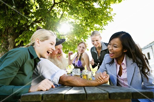 Asian woman and man in Bavarian dress in beer garden, arm wrestling