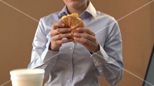 Young woman eating croissant filled with scrambled egg