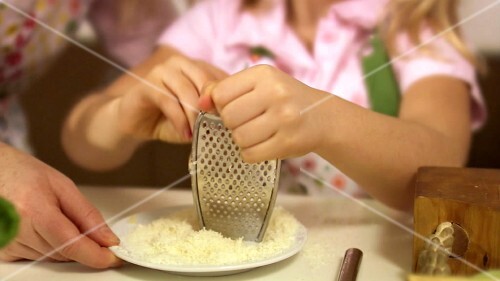 Tochter reibt Käse, Mutter probiert Käseraspel