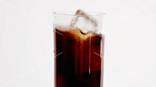Pouring cola into a glass and adding ice cubes