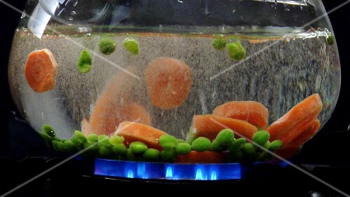 Peas and carrot slices being dropped into hot water