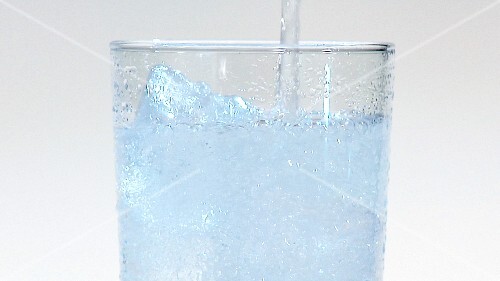 Pouring mineral water into a glass of ice cubes (close-up)