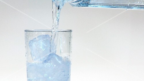 Pouring mineral water into a glass of ice cubes