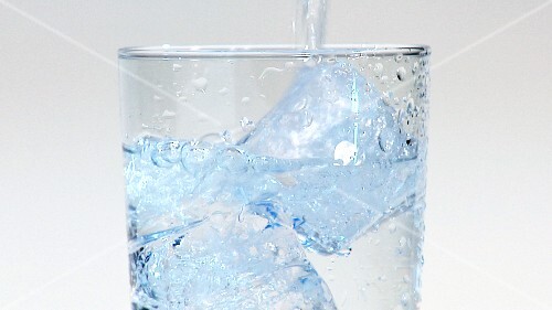 Pouring water into a glass of ice cubes (close-up)