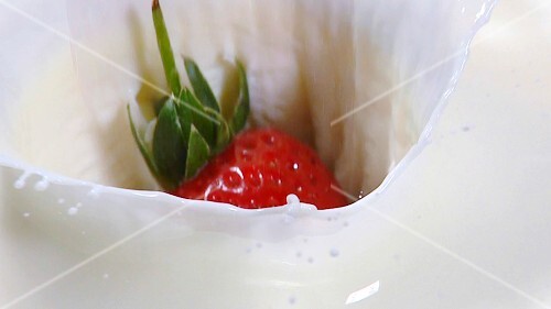 Eine Erdbeere fällt in Milch