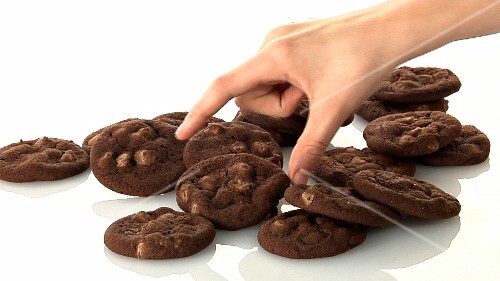 A pile of chocolate chip cookies and a hand taking one