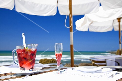 Sangria with berries in jug & sparkling wine glass on table by sea