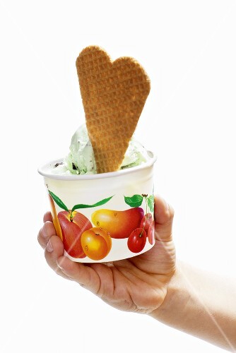 Hand holding cardboard tub of peppermint ice cream with wafer