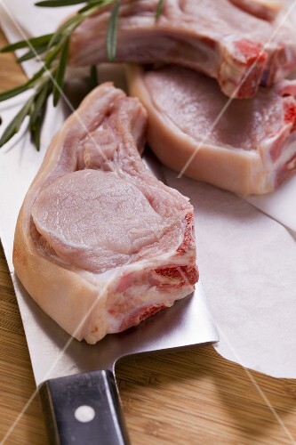 Raw pork chops with meat cleaver and rosemary