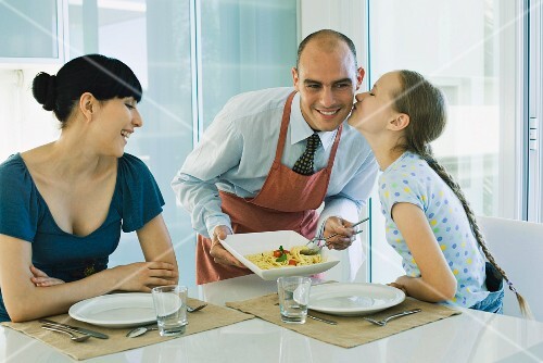 Man serving wife and daughter spaghetti, girl kissing father on cheek