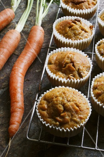 Carrot muffins on a wire rack with carrots next to them