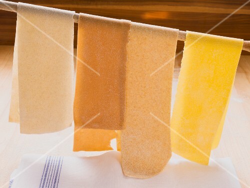 Sheets of pasta hanging from a wooden spoon to dry