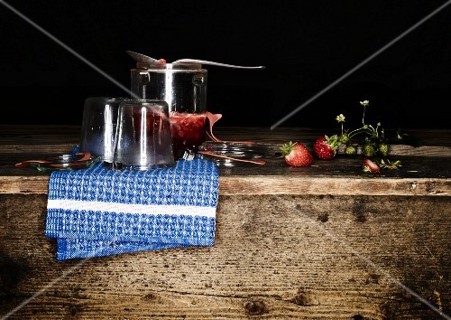 Jam jars, strawberry jam, spoons and strawberries on a wooden board