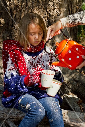 A hot drink being poured into a mug held by little girl