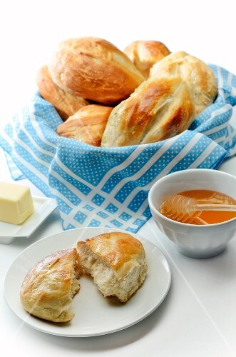 Basket of Bolillo Rolls; One on a Plate Halved; Honey in a Bowl