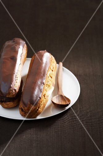 Two chocolate eclairs on a plate with a wooden spoon