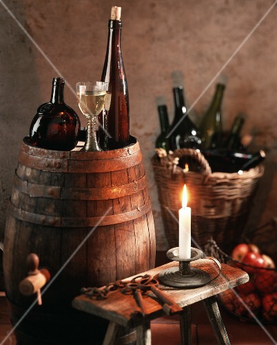 Stilleben im Weinkeller mit Wein auf Fass und im Korb; Kerze