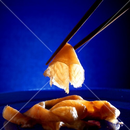 Raw salmon slices on blue plate and between chopsticks
