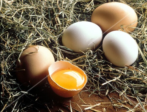 Brown and white eggs with a broken egg in hay