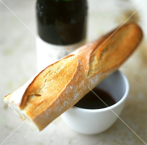 Baguette on coffee cup in front of red wine bottle