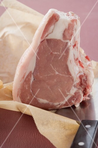 Raw veal loin steak on greaseproof paper with cleaver