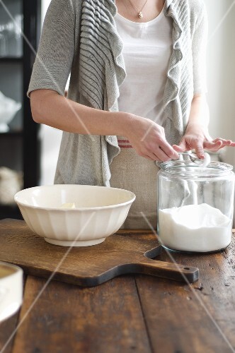 Woman taking a measuring spoonful of sugar from storage jar