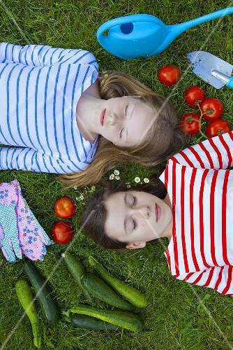 Two girls lying on the grass surrounded by vegetables
