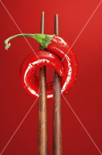A chilli on chopsticks, red background