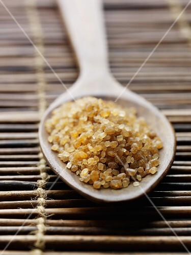 Raw cane sugar in a wooden spoon on a bamboo mat