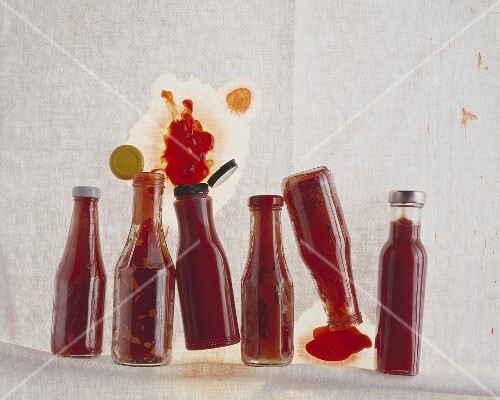 Several closed & opened ketchup bottles, lying on their sides