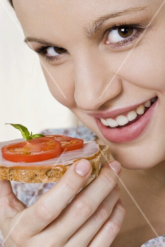 Junge Frau isst Vollkornbrot mit Schinken und Tomaten
