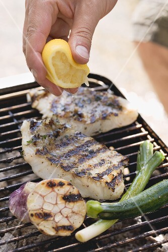 Hand squeezing lemon juice over grilled fish fillets