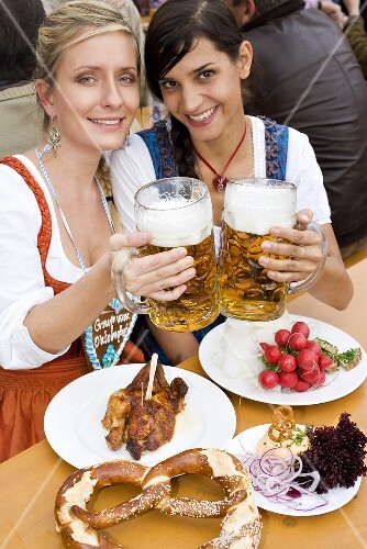 Two women with typical snacks clinking tankards of beer (Oktoberfest)