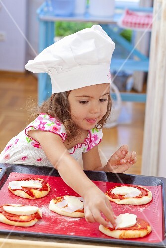 A little girl placing toppings on a pizza
