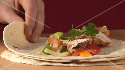 Rolling up a tortilla filled with chicken breast and salsa