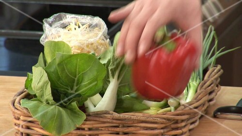 Hand taking red pepper & carrot out of basket of vegetables